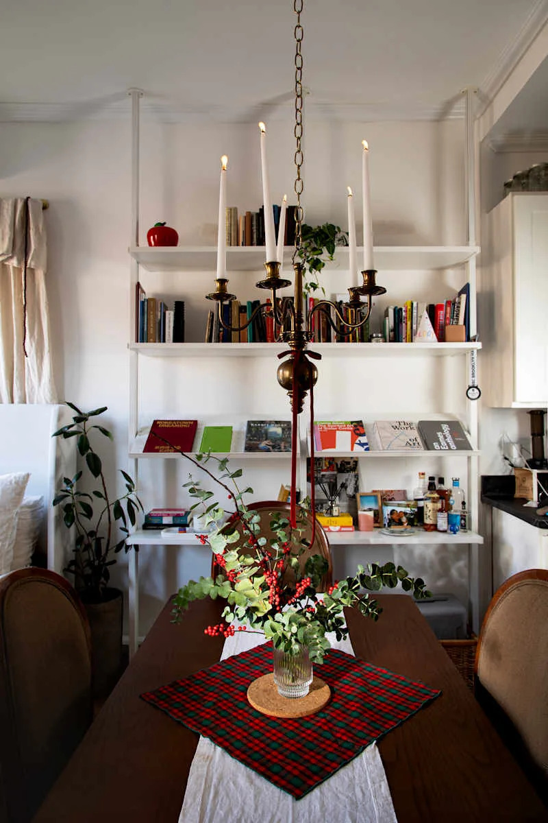 Dining table with a plaid tablecloth, floral centerpiece, and a chandelier above; bookshelves in the background.