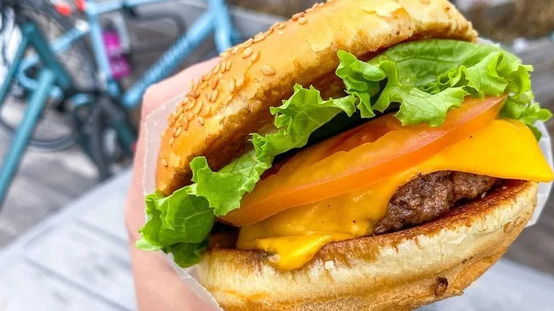 A hand holding a sesame seed burger with cheese from F. Ottomanelli in NYC