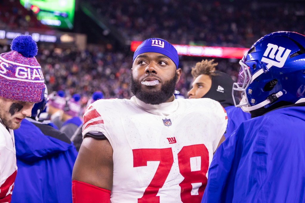 New York Giants offensive tackle Andrew Thomas #78 wearing a white and red jersey and blue beanie with the NY logo on it, reacts on the sideline.
