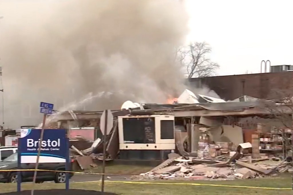 A nursing home building, "Bristol Health & Rehab Center," damaged by an explosion with smoke rising and debris scattered.