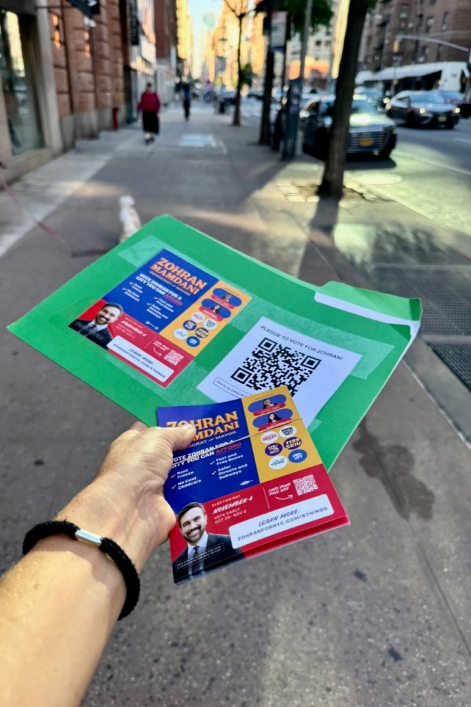 A hand holds an election flyer for Zohran Mamdani