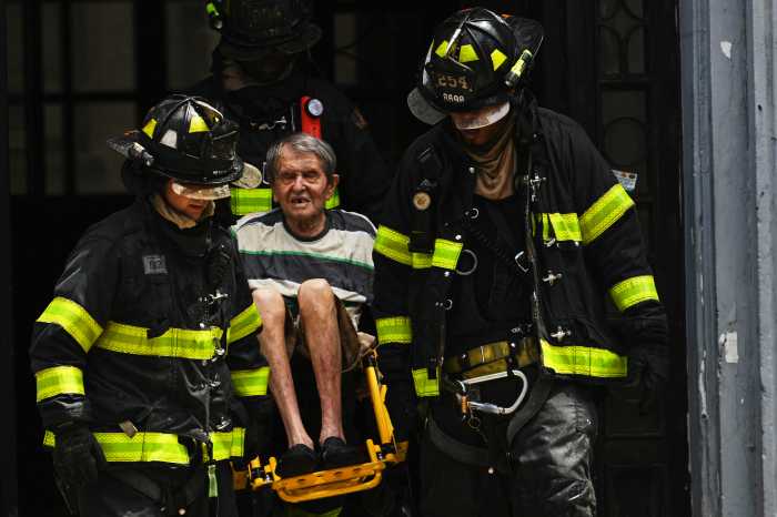 firefighters helping to carry man out of burning building