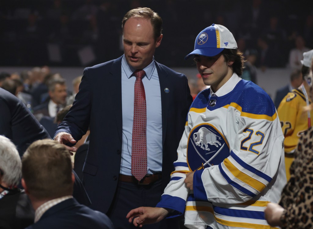 General manager Kevyn Adams of the Buffalo Sabres (L) introduces Matthew Savoie to team personnel at their draft table 