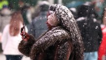 A woman uses her smartphone during a snowfall in Times Square on December 26, 2025, in New York City. New York, the US largest city, was bracing for up to 10 inches (25 centimeters) of snow overnight, the most in four years. (Photo by TIMOTHY A. CLARY / AFP via Getty Images)