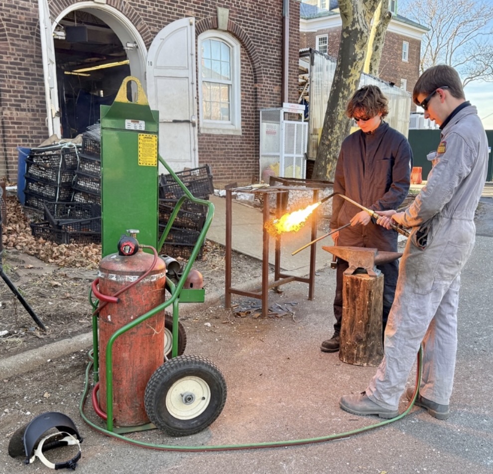 Harbor School students work with fire and metal outside a brick workshop. (Credit: Baron Carr)