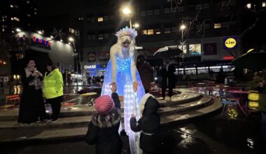 Brianna Kalisch, a circus variety performer, greets two children during a tree lighting ceremony on a rainy night in Downtown Brooklyn. (Credit: Loyalty Jean Aimé)