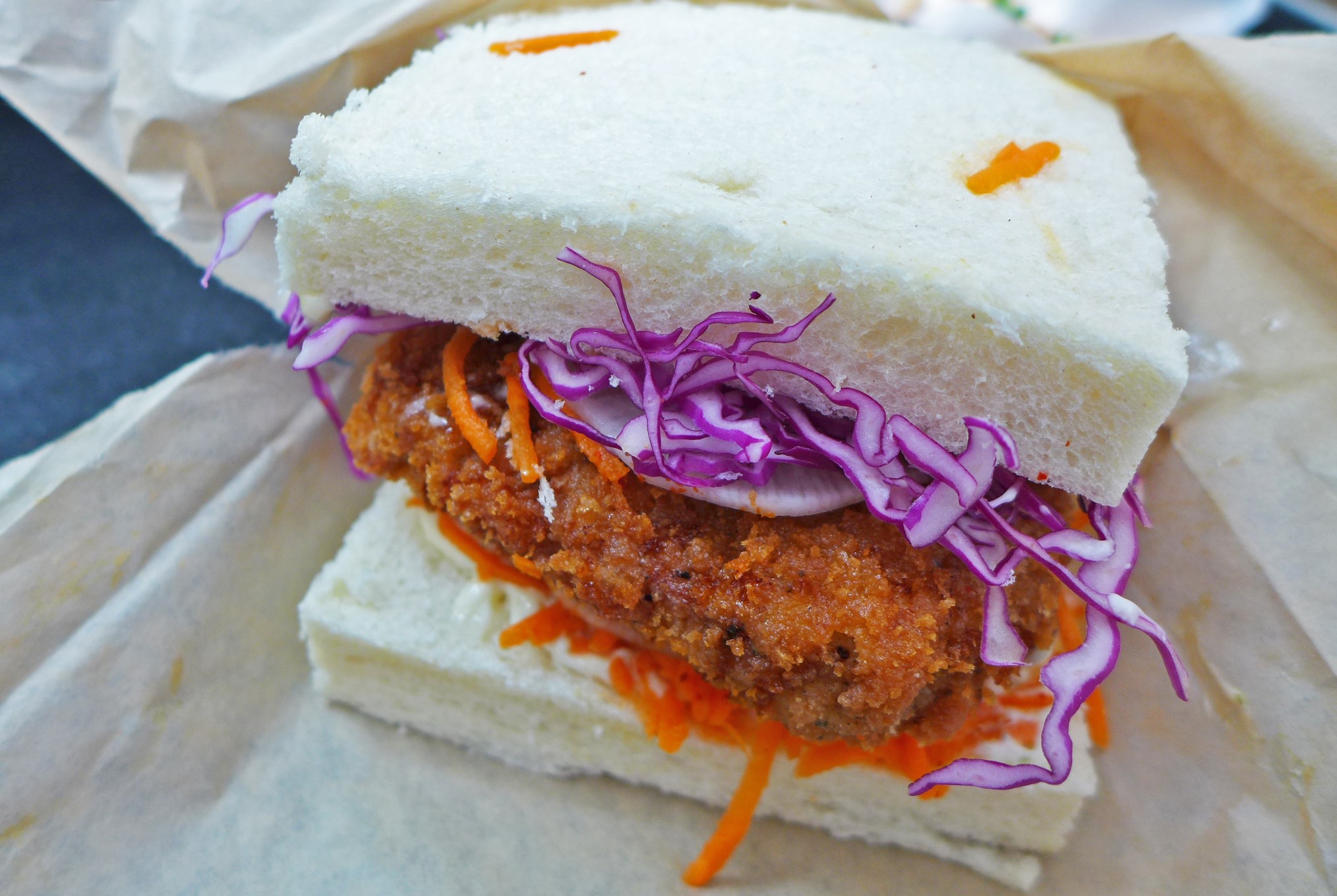 Two square slices of white bread with a crumbed cutlet and orange and purple slaw.