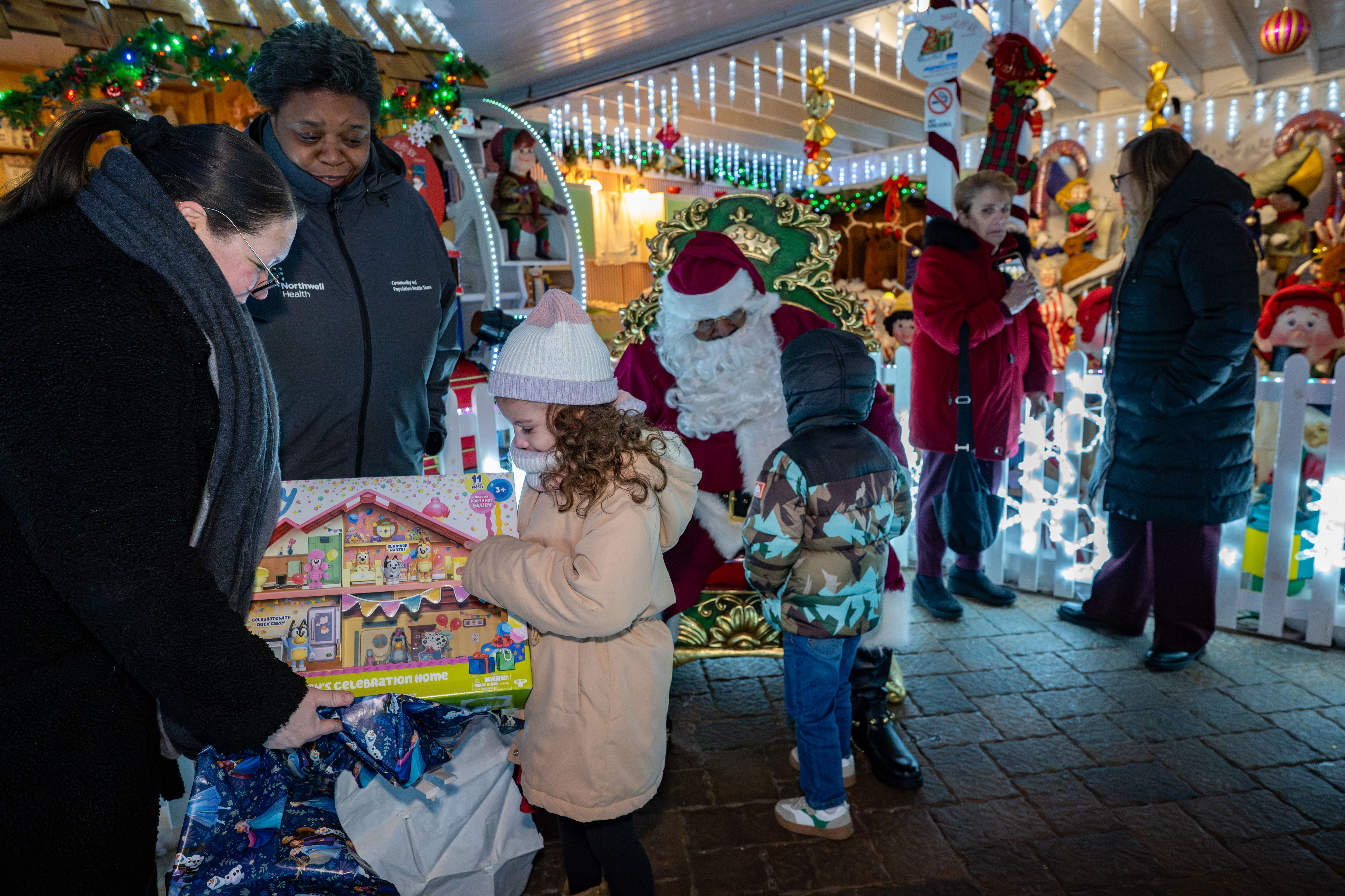 Taisha Figueroa, a Northwell Staten Island University Hospital employee who is being honored with a Day of Surprises, helps her granddaughter, Julissa Irrizarry, 6, open gifts at the DeMartino Christmas House in Charleston on Tuesday, December 16, 2025. Look on is Claudette Hill from the hospital's Community and Population Health Team. (Owen Reiter for the Advance/SILive.com)