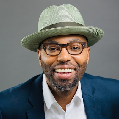 A man in a fedora smiles. 