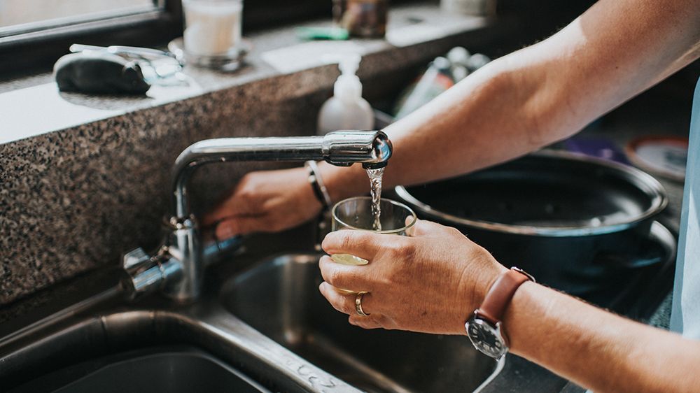 Person at a tap, filling a glass of water.