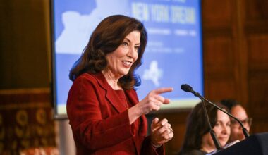 kathy hochul smiles and points from a podium during a press conference
