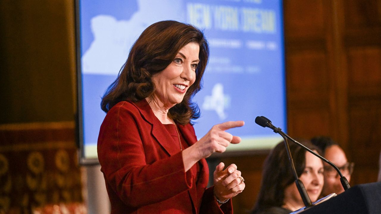 kathy hochul smiles and points from a podium during a press conference
