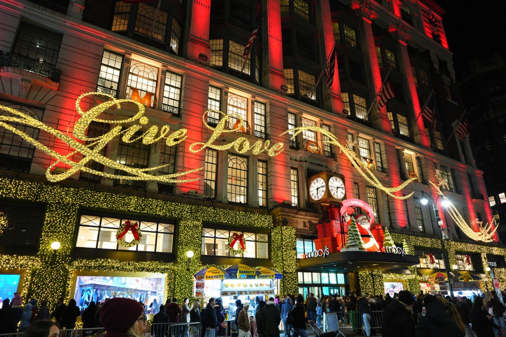 Black Friday shoppers gather outside Macy's in Herald Square, lit up with holiday decorations including a "Give Love" sign.