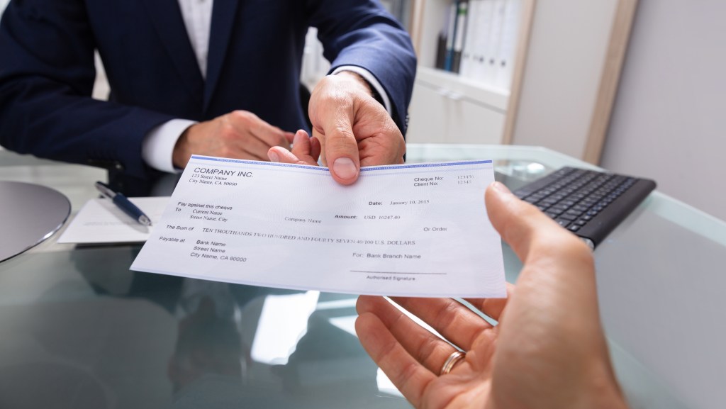 A businessman in a suit handing a check to another person.