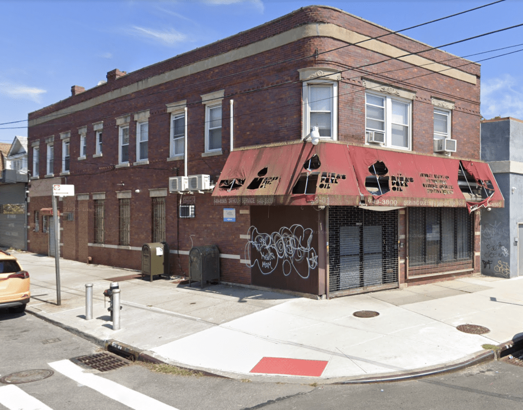 A brick building with a damaged red awning at the corner of a street.