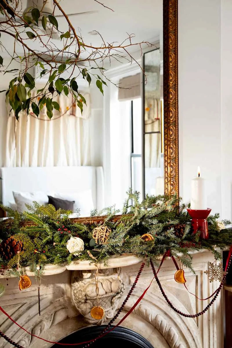 Festively decorated mantel with greenery, pinecones, dried orange slices, and a red candle, reflecting a cozy atmosphere.