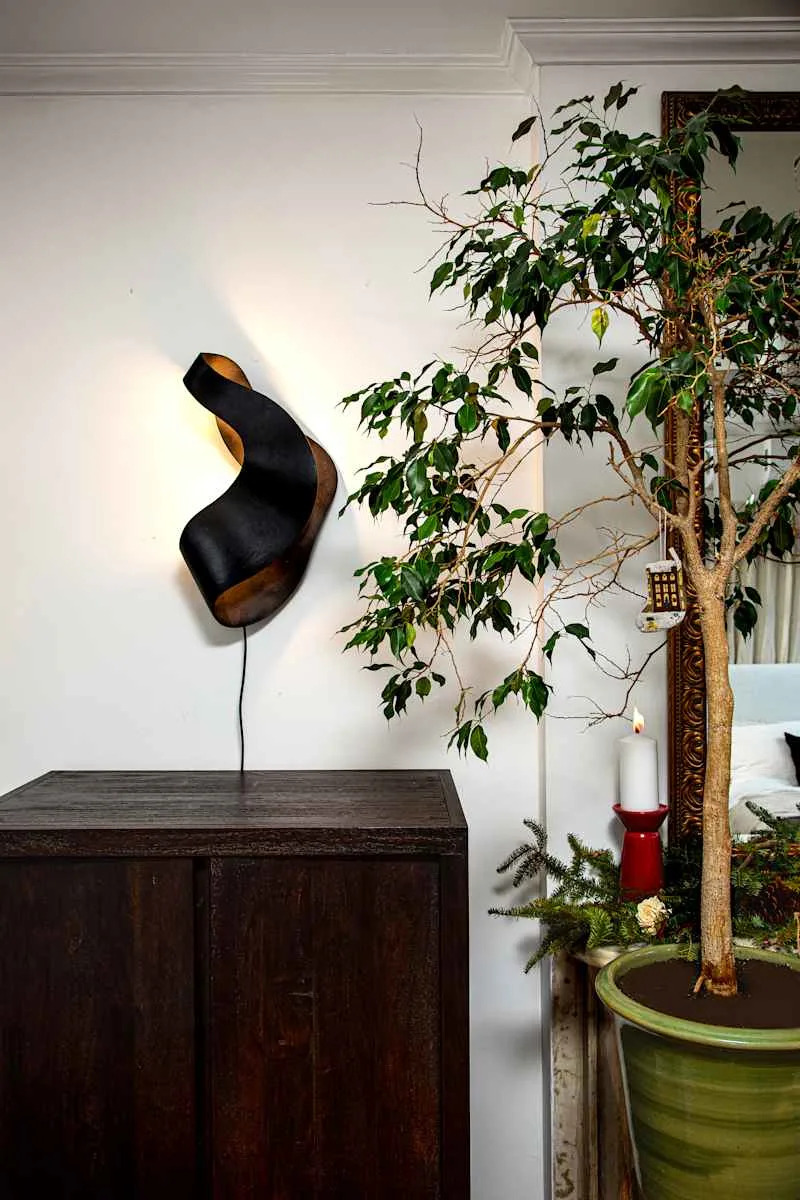 A modern black wall lamp above a dark wooden cabinet, next to a potted tree with green leaves and a candle.