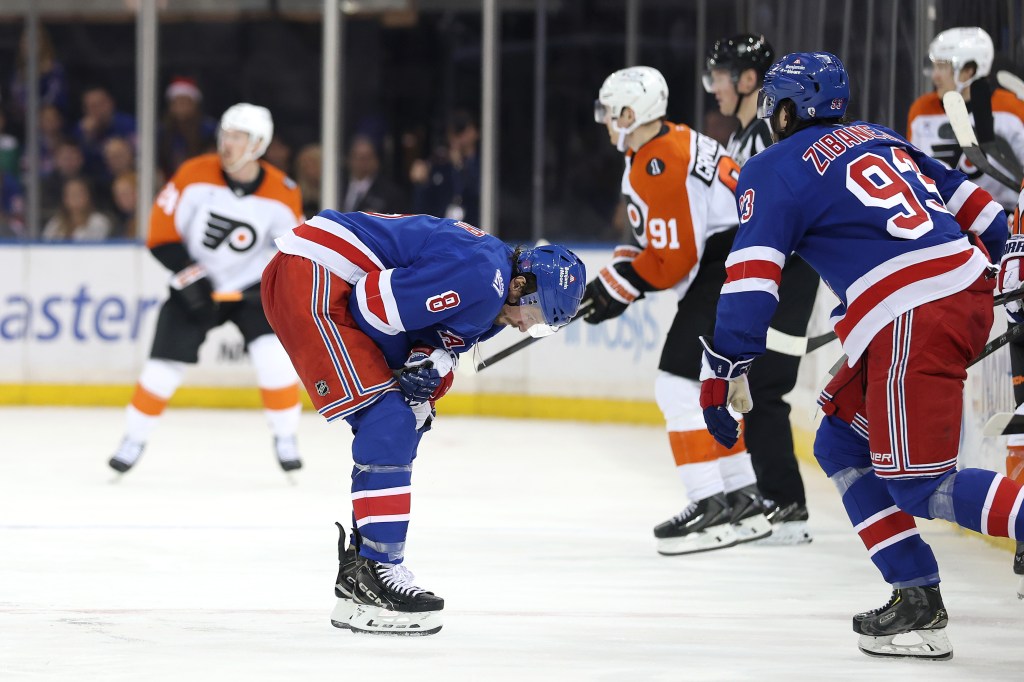 New York Rangers player J.T. Miller bends over on the ice, appearing injured, surrounded by other players.