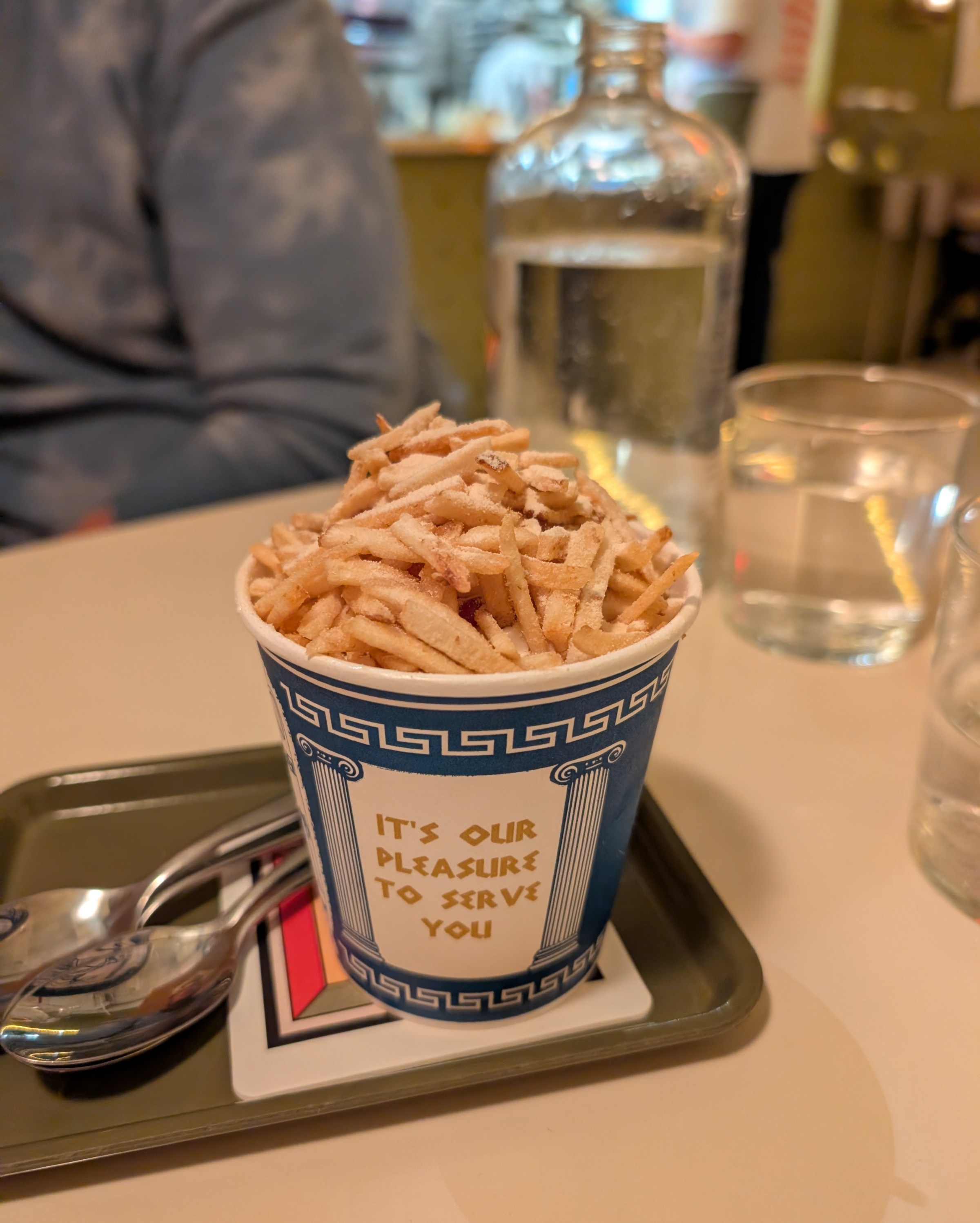 A blue-and-white coffee cup with thin fries on top of it.