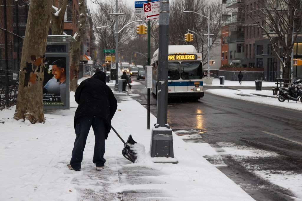 A man shovels snow from a sidewalk in New York City in Dec 2024