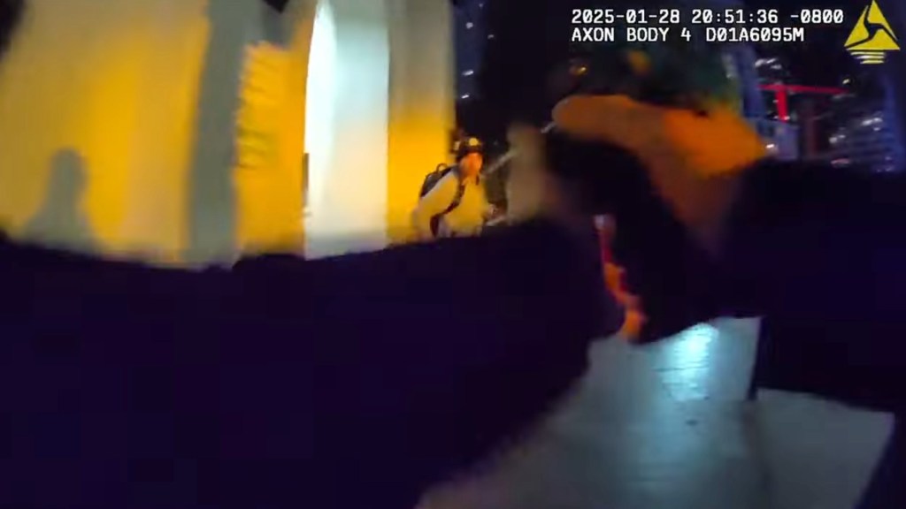 Still from bodycam footage showing a police officer's arm and gun aimed at a fleeing Black teen at night.