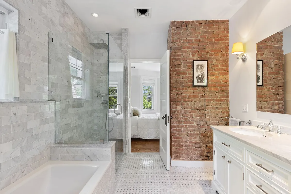 bathroom with white fixtures, one corner wall of exposed brick