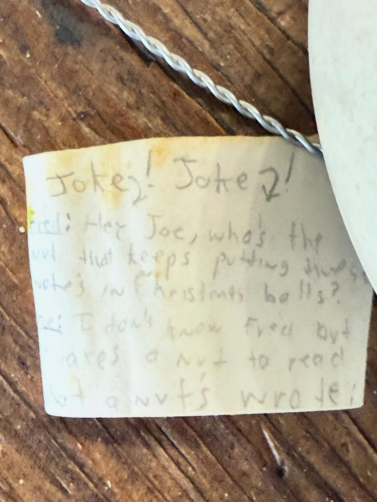 A slip of paper with a handwritten joke: "Hey Joe, who's the nut that keeps putting these notes in Christmas bells? I don't know Fred but who cares, a nut wrote it."