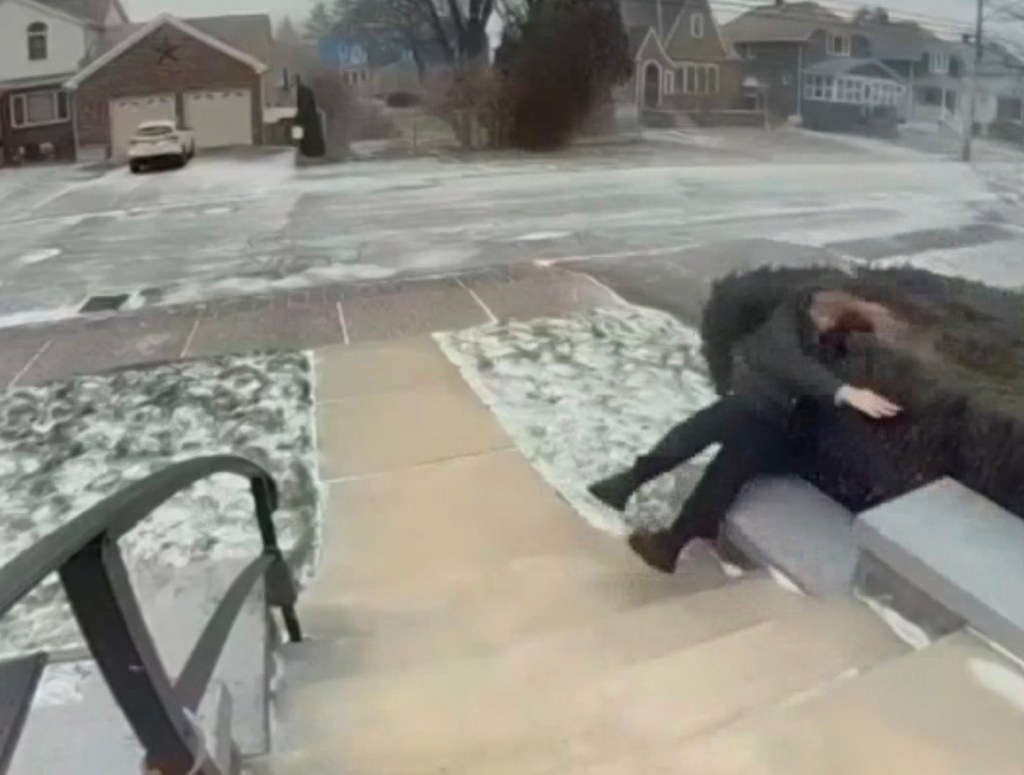 Person blown over by wind into a bush next to a snowy sidewalk.