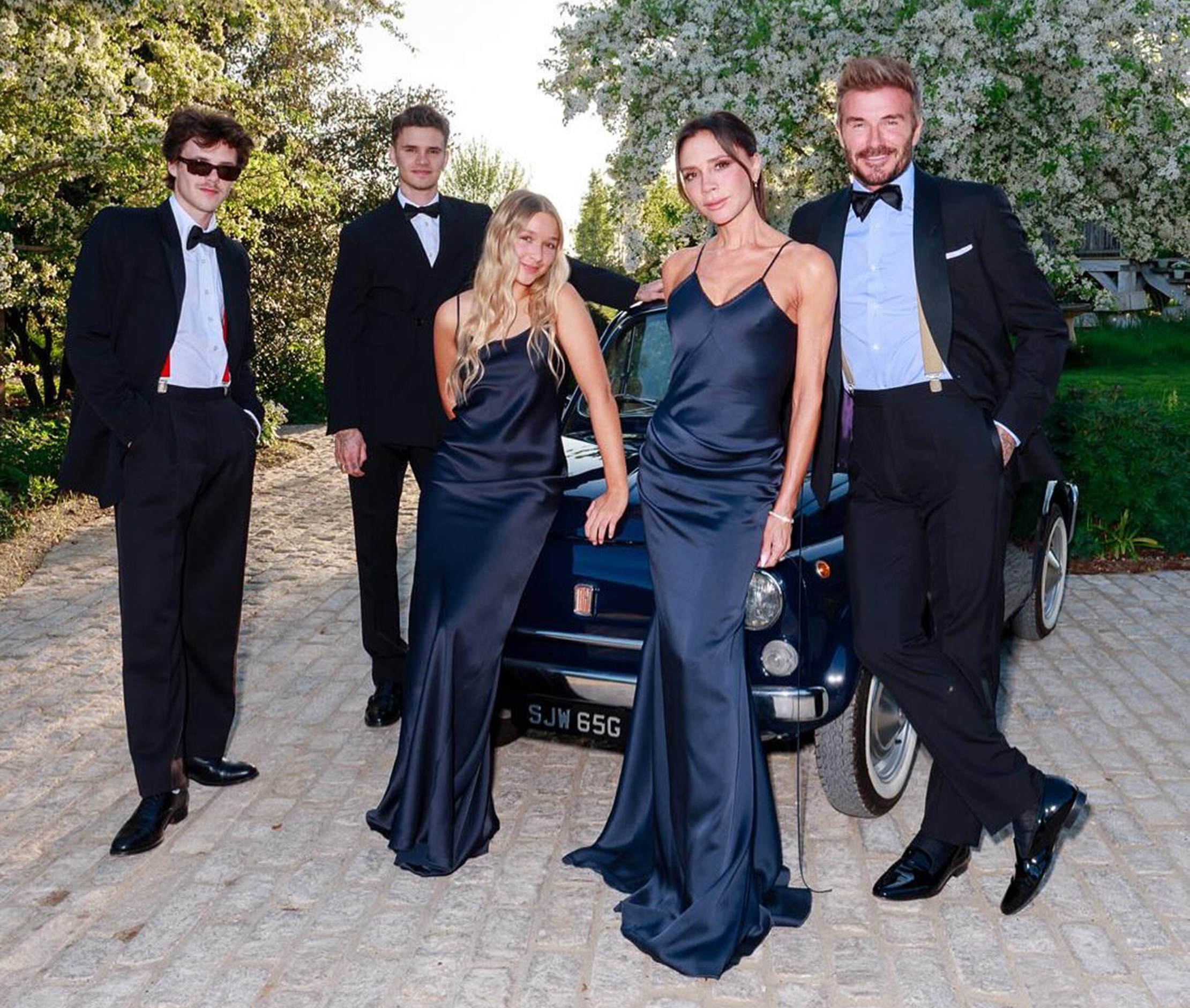 The Beckham family, dressed in formal attire, poses with a car.
