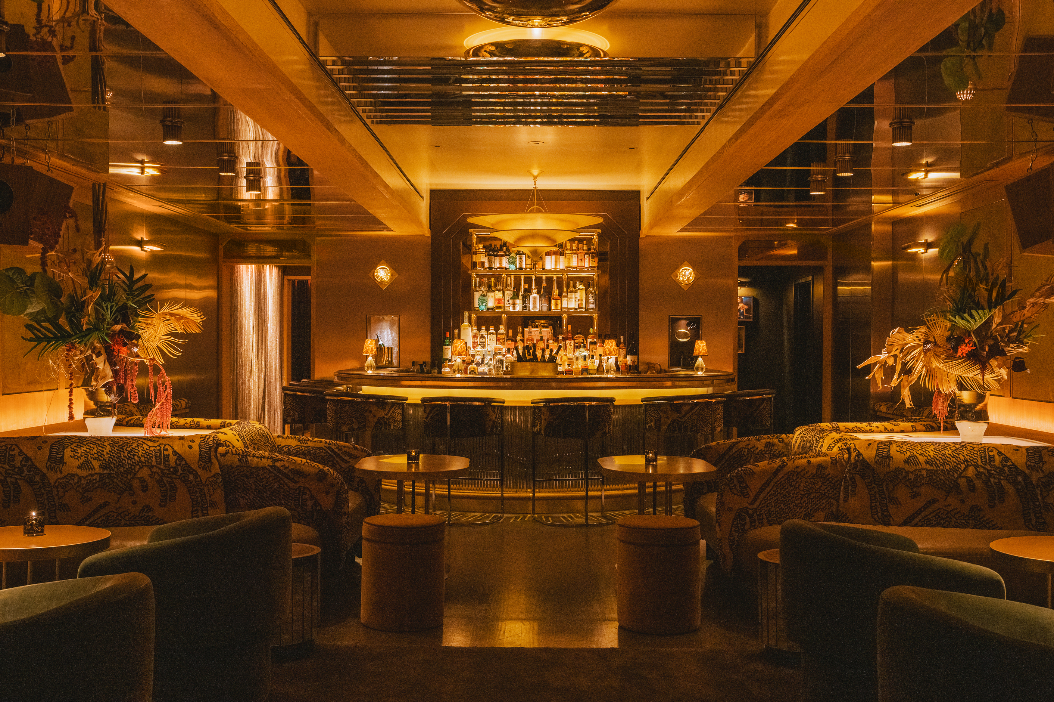 Interior of a dimly lit, luxurious bar with a mirrored ceiling, a fully stocked bar, and lounge seating.