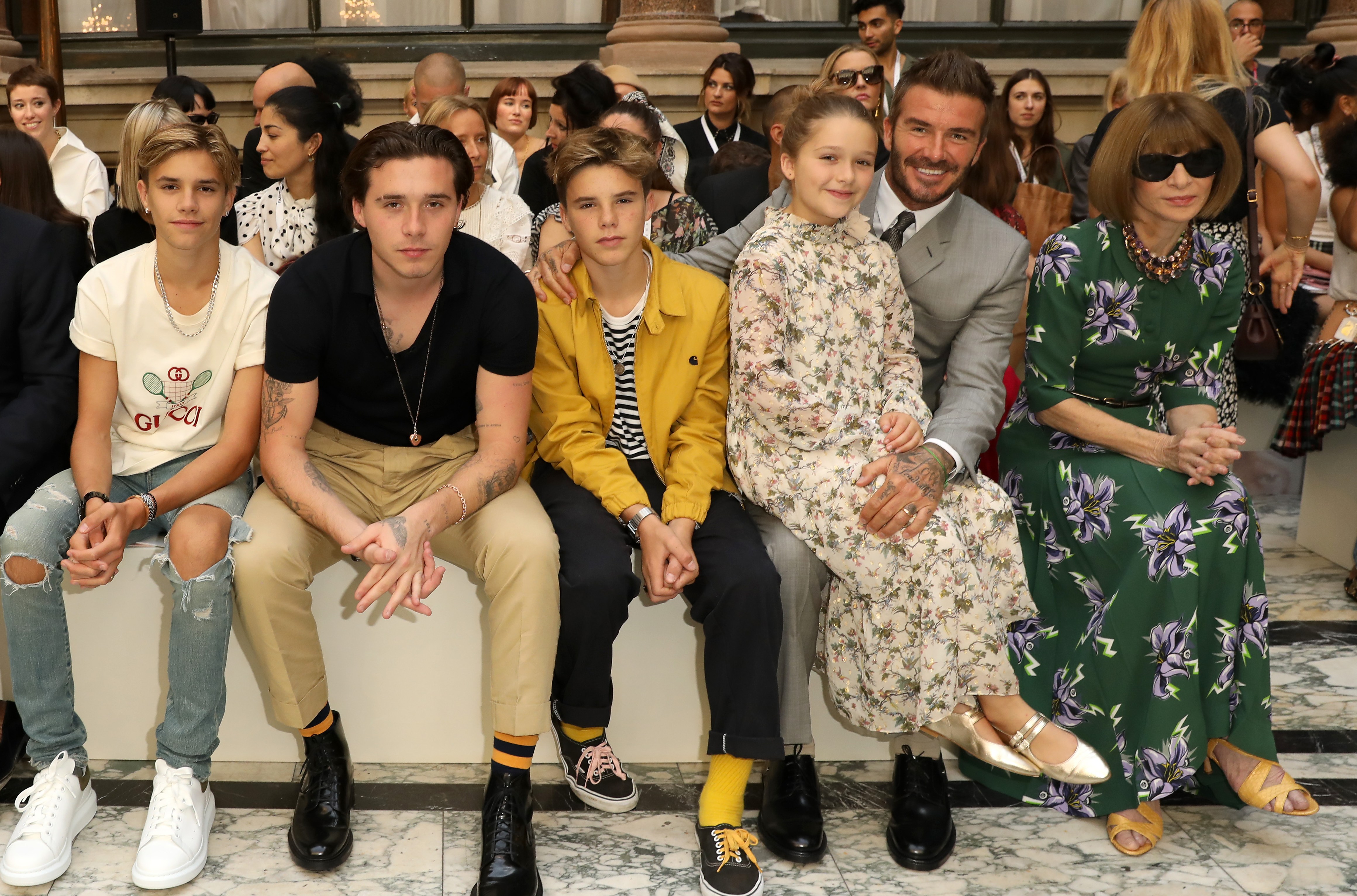 Emmanuelle Alt, Edward Enninful, Romeo Beckham, Brooklyn Beckham, Cruz Beckham, Harper Beckham, David Beckham and Anna Wintour sitting in the front row at a fashion show.