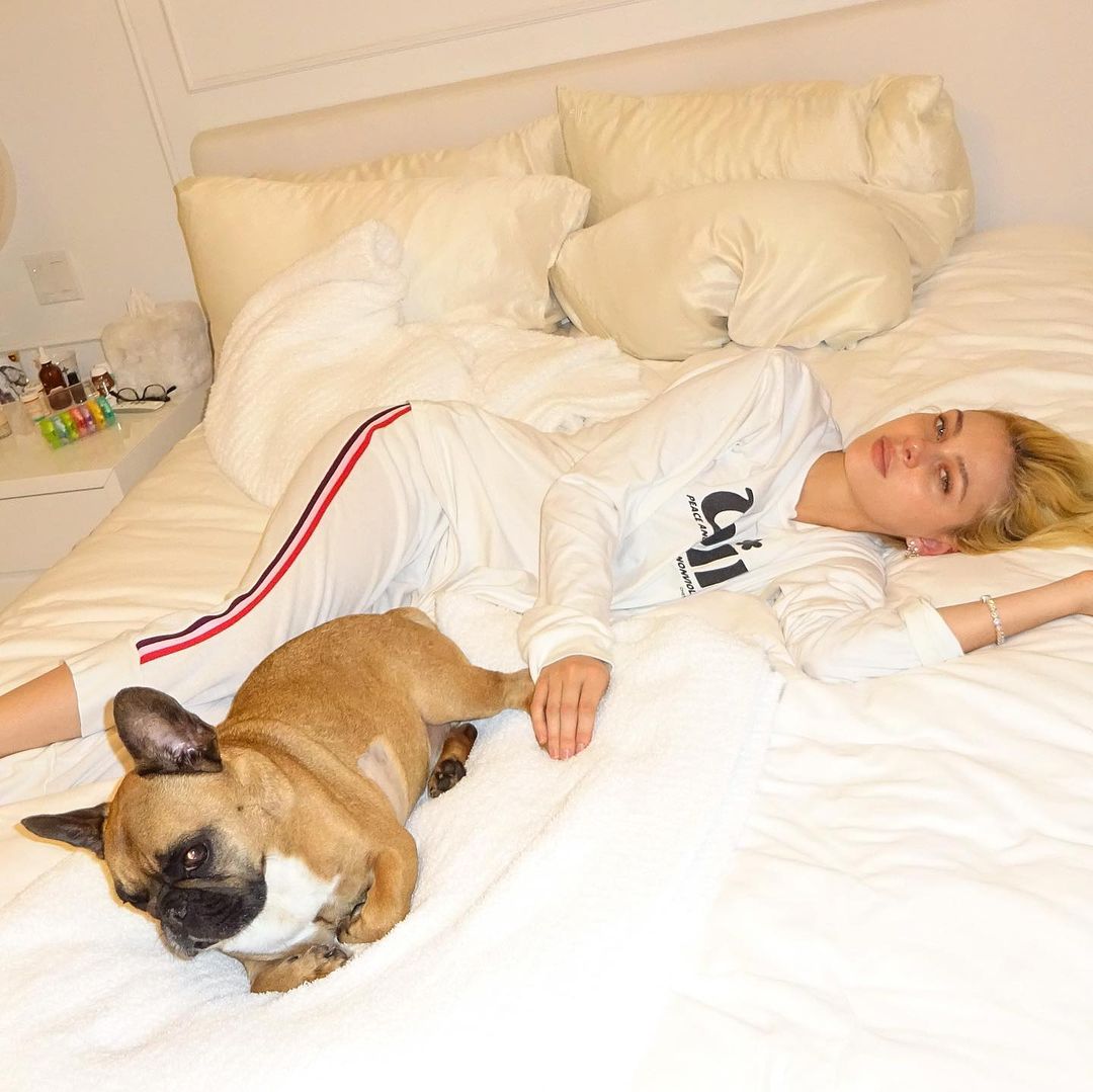 Nicola Peltz and her French bulldog, Frankie, lie on a white bed.