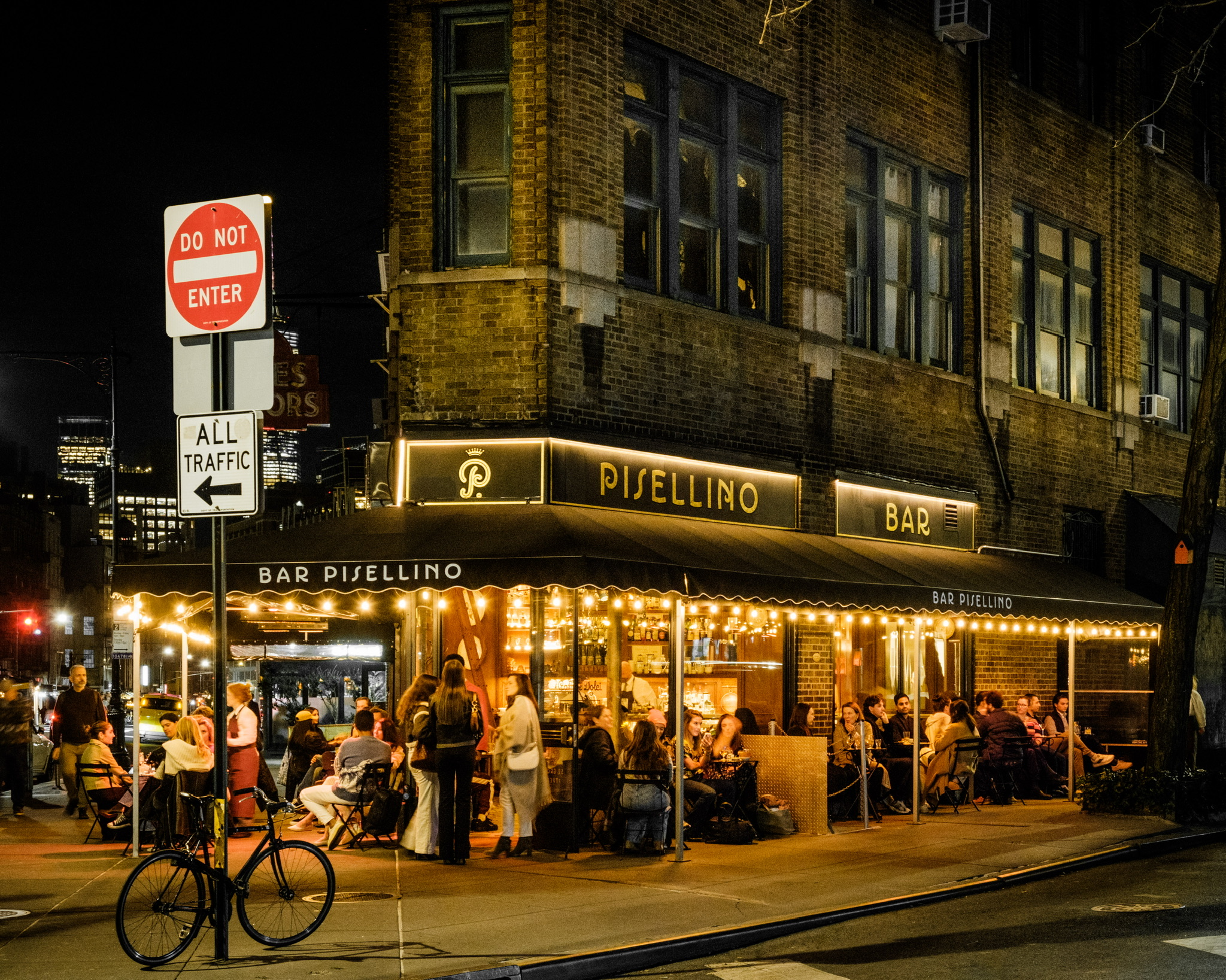 Exterior night shot of Bar Pisellino with people dining al fresco.