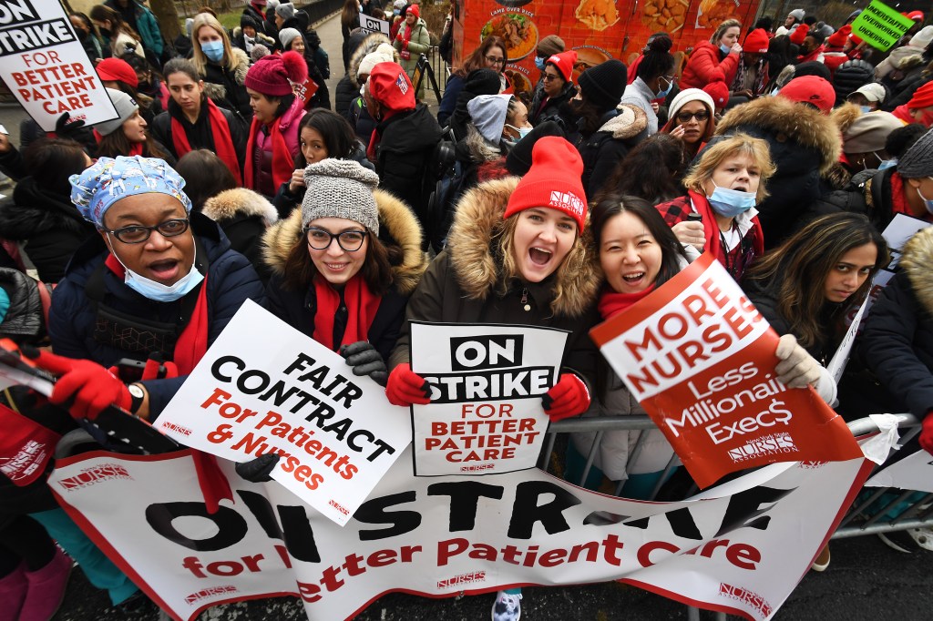Nurses from the New York State Nurses Association (NYSNA) on strike with signs that say "Fair Contract for Patients & Nurses," "On Strike for Better Patient Care," and "More Nurses, Less Millionaire Execs."