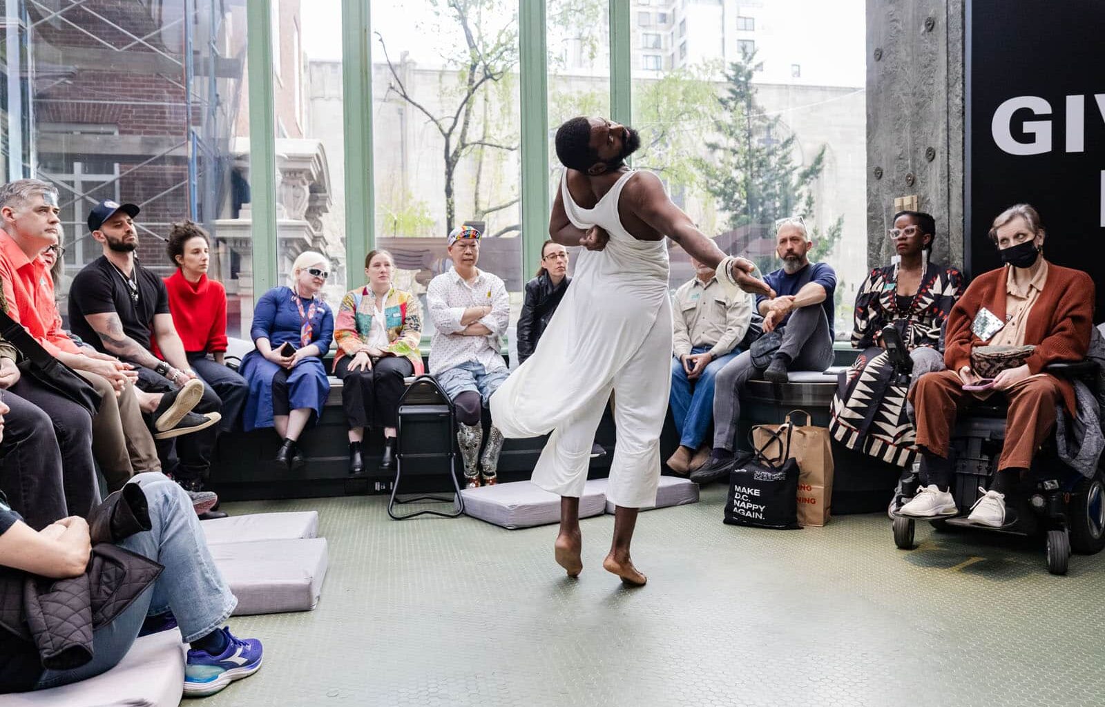 Alameda Post - Jerron Herman twirls in mid-turn dressed in a long, flowy white tunic in front of the audience in a light-filled atrium.