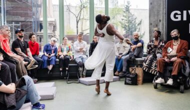 Alameda Post - Jerron Herman twirls in mid-turn dressed in a long, flowy white tunic in front of the audience in a light-filled atrium.