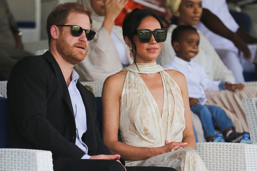 A man and a woman in sunglasses sit in the stands of a stadium