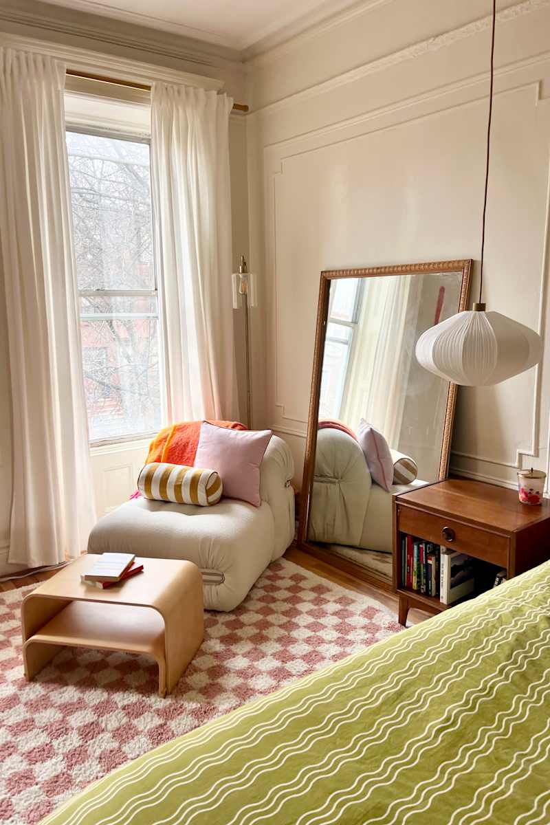 Cozy bedroom corner with a large mirror, a plush chair with colorful pillows, a wooden side table, and a patterned rug.