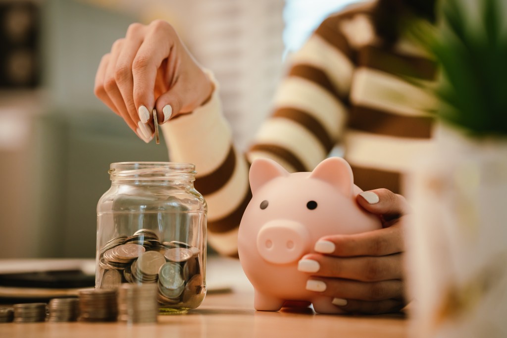 A woman's hand putting a coin into a piggy bank.