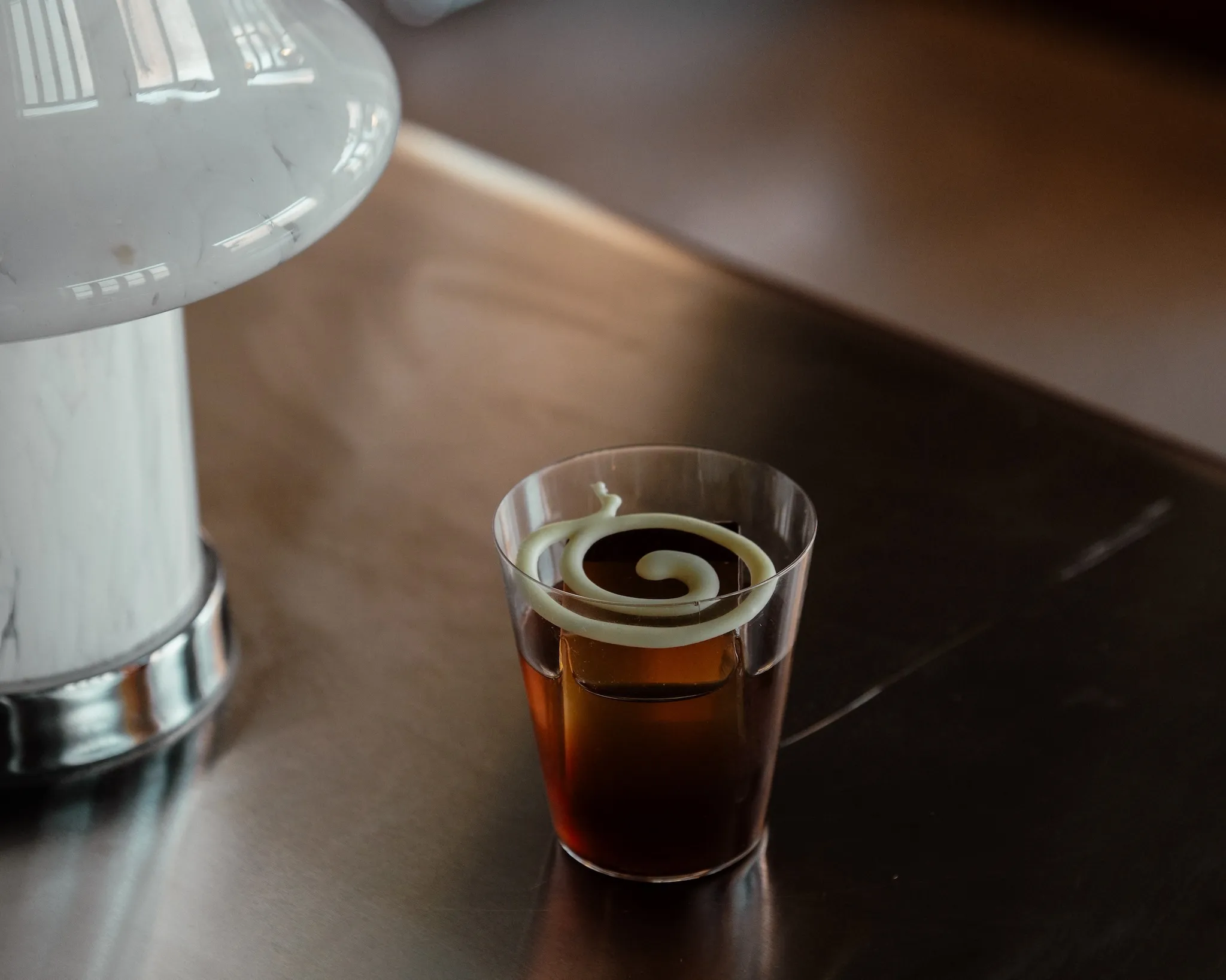 A brown cocktail with a swirl on top