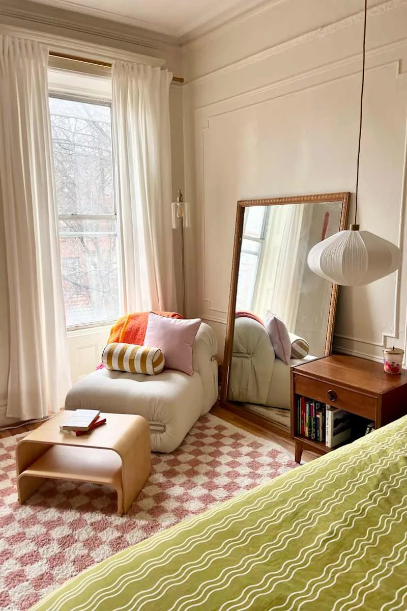 Cozy bedroom corner with a large mirror, a plush chair with colorful pillows, a wooden side table, and a patterned rug.