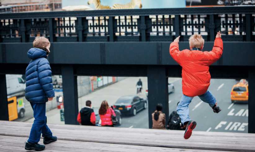 Two boys wearing winter jackets and jumping along the High Line