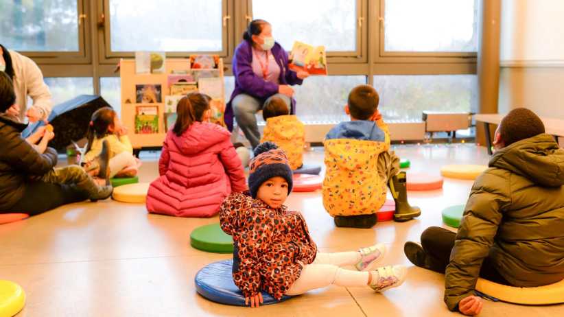 children sitting listening to a women reading a picture book.