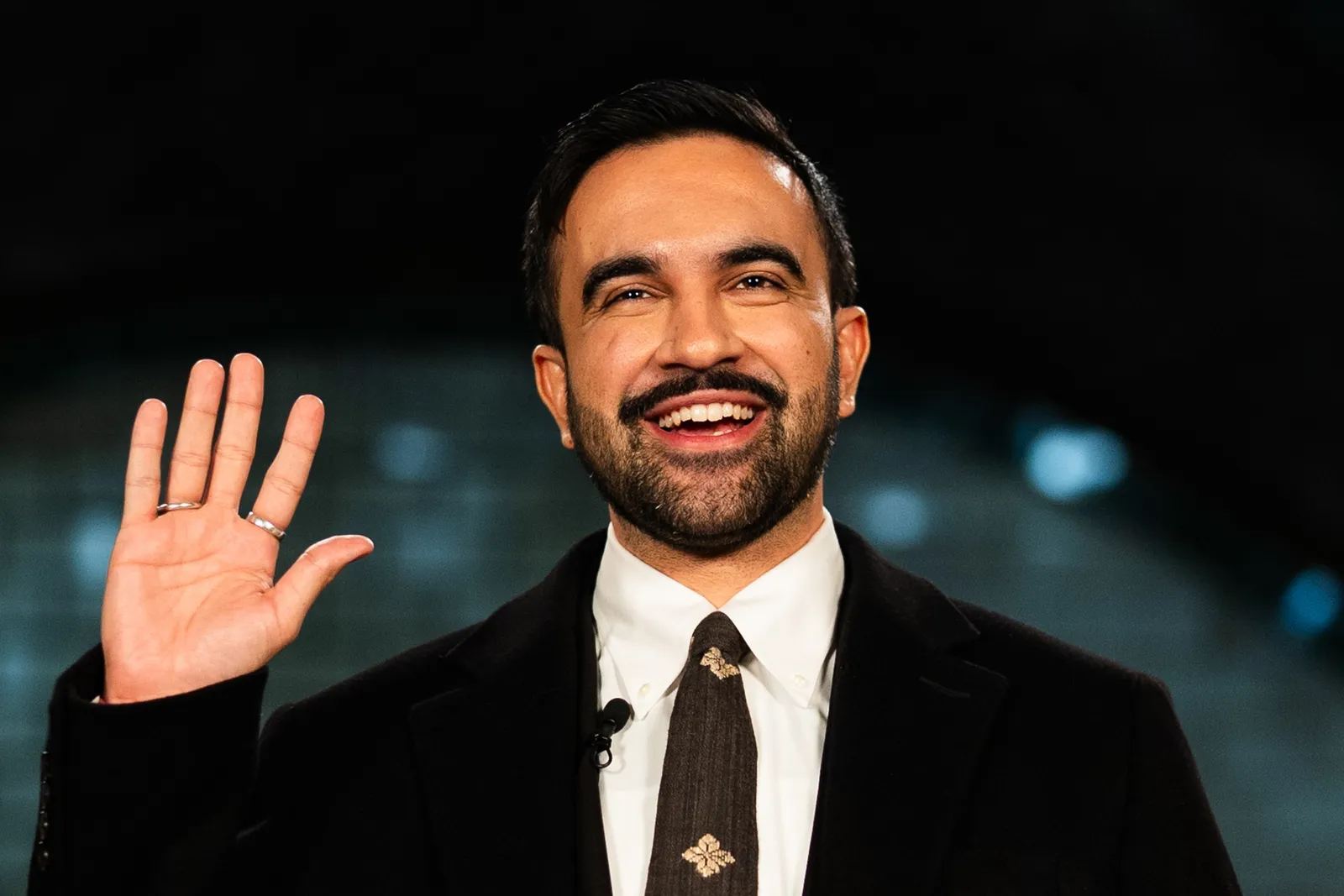 Image may contain Head Person Face Happy Smile Dimples Adult Clothing Coat Accessories Formal Wear and Tie