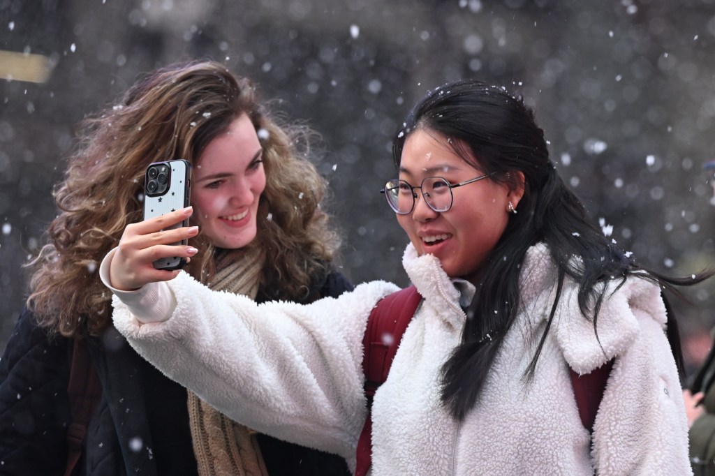 Two women smile while taking a selfie in a mid-January snowstorm in Midtown NYC.