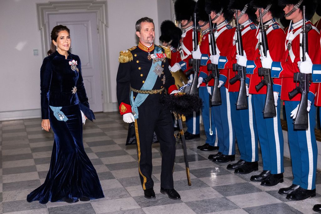 queen Mary in navy dress beside king frederik in uniform with soldiers standing to attention in palace