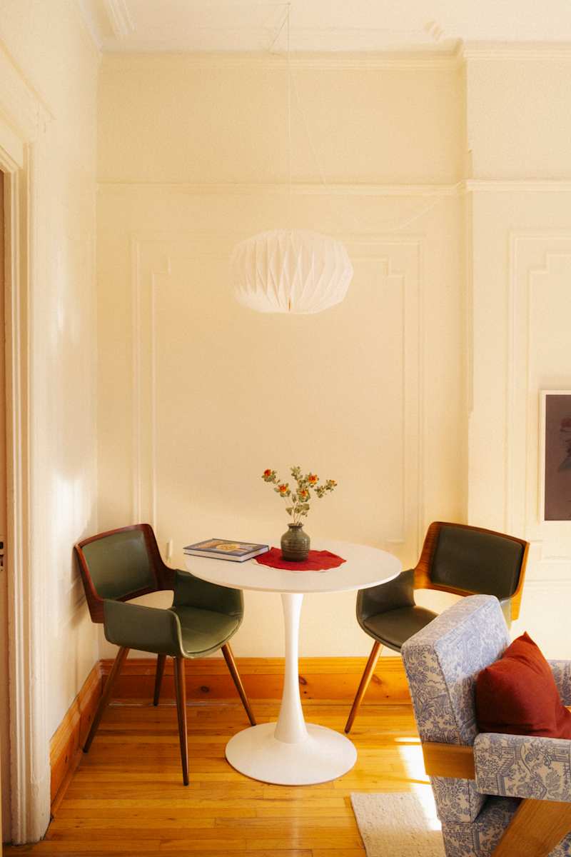 Cozy dining nook with a round white table, two green chairs, a vase of flowers, and a patterned blue sofa.