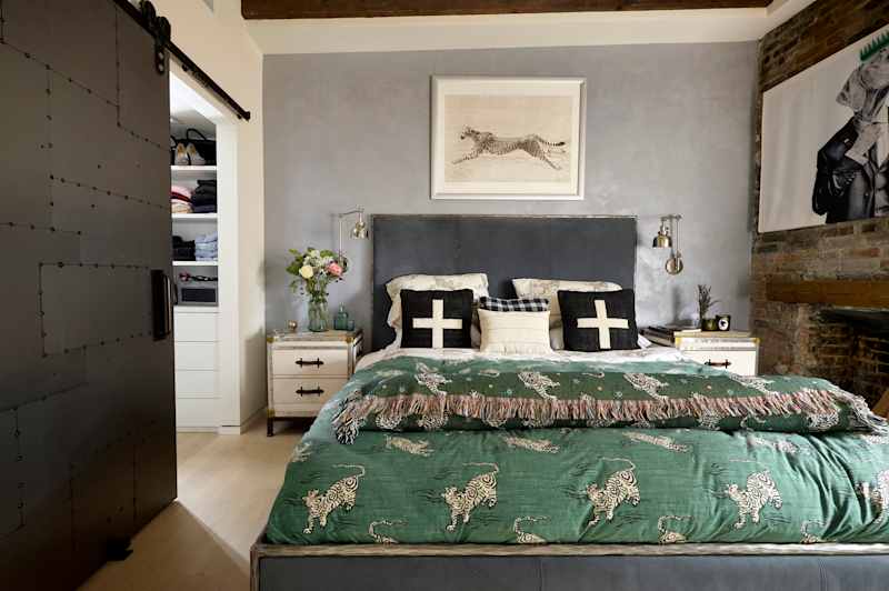 Cozy bedroom featuring a green patterned duvet, black and white pillows, a floral vase, and a sliding barn door.