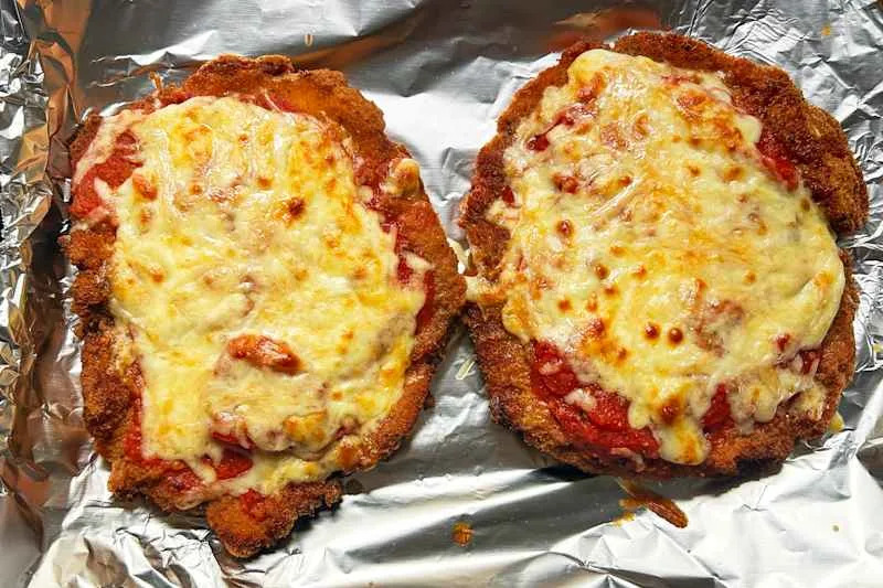 Two breaded chicken cutlets topped with marinara sauce and melted cheese.
