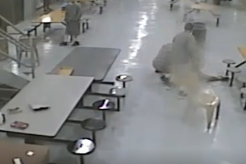 A still from CCTV footage showing a grey communal area in a prison with several inmates attacking another inmate.